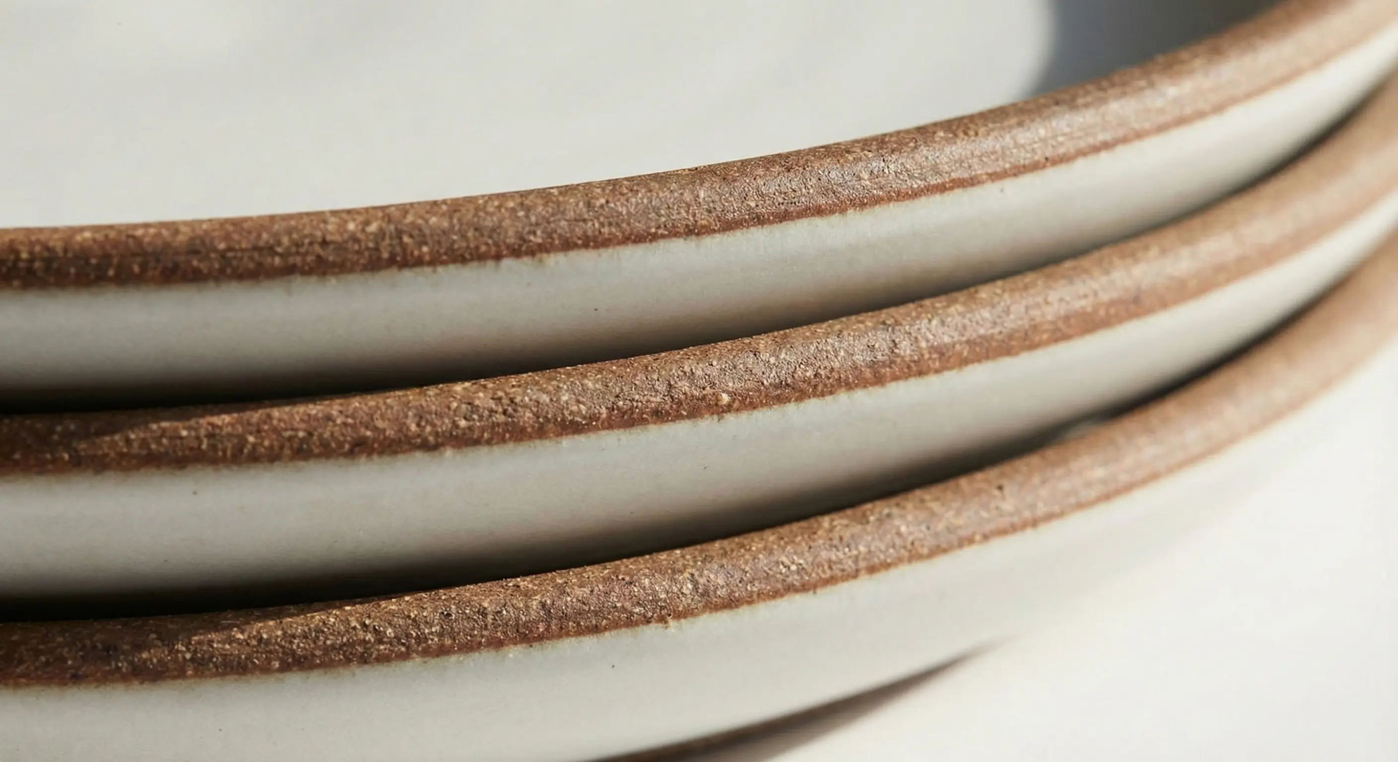 Close-up shot of stacked Heath Ceramics coupe plates showing the exposed clay rim and matte glaze.